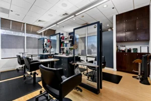 Modern hair salon interior with black styling chairs, workstations with mirrors, shelves of hair products, and natural light from large windows with blinds. - Get Panache, FL