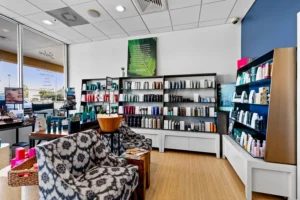 The retail area at our St. Augustine Aveda Salon features patterned armchairs, display shelves with beauty products, a wooden floor, and a large window that fills the space with natural light. - Get Panache, FL