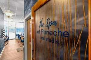 Entrance to a nail studio and spa with a sign on the door reading "The Spa at Panache nail studio," showing a bright, modern interior with chandeliers and salon chairs. - Get Panache, FL