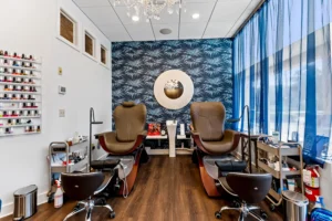 Two pedicure chairs with footbaths are positioned in a nail salon, featuring a blue patterned accent wall, nail polish display, and floor-to-ceiling blue curtains—an inviting space also known for highly-skilled lash extensions St. Augustine. - Get Panache, FL