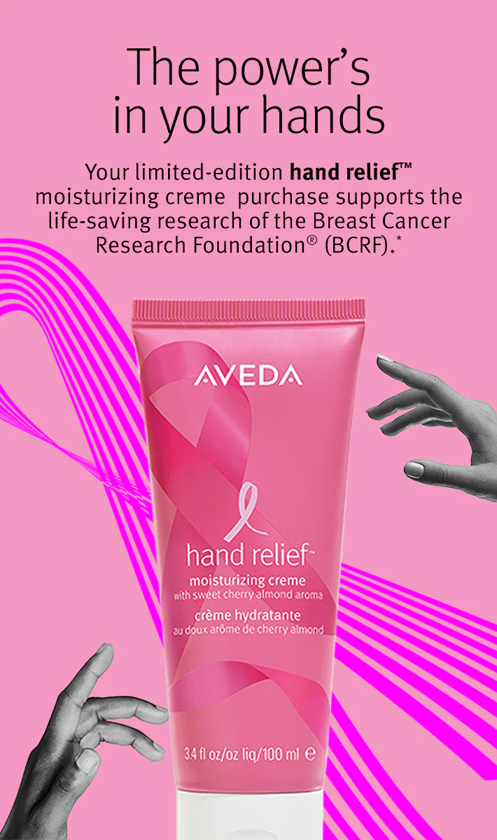 A pink tube of Aveda hand relief moisturizing creme with breast cancer ribbon, text about supporting the Breast Cancer Research Foundation, and a hand reaching in from the side. - Get Panache, FL
