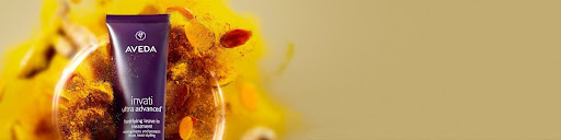 Aveda Invati Advanced hair product tube is displayed upright in front of a background featuring yellow and orange botanical elements, perfect for Holiday Event Hair and seasonal Fall Style Tips. - Get Panache, FL