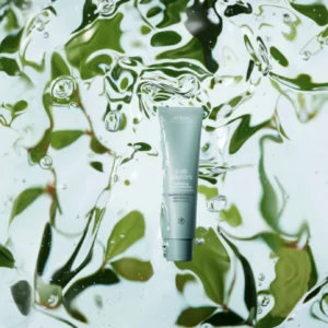 Aveda Scalp Solutions tube, featuring Aveda Advanced Botanical Kinetics, is suspended in clear water with green leaves visible through the water in the background. - Get Panache, FL